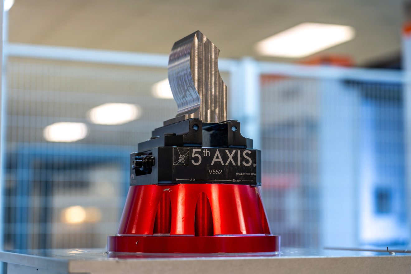 Machined part on a red 5-axis trunnion fixture inside a CNC machining center