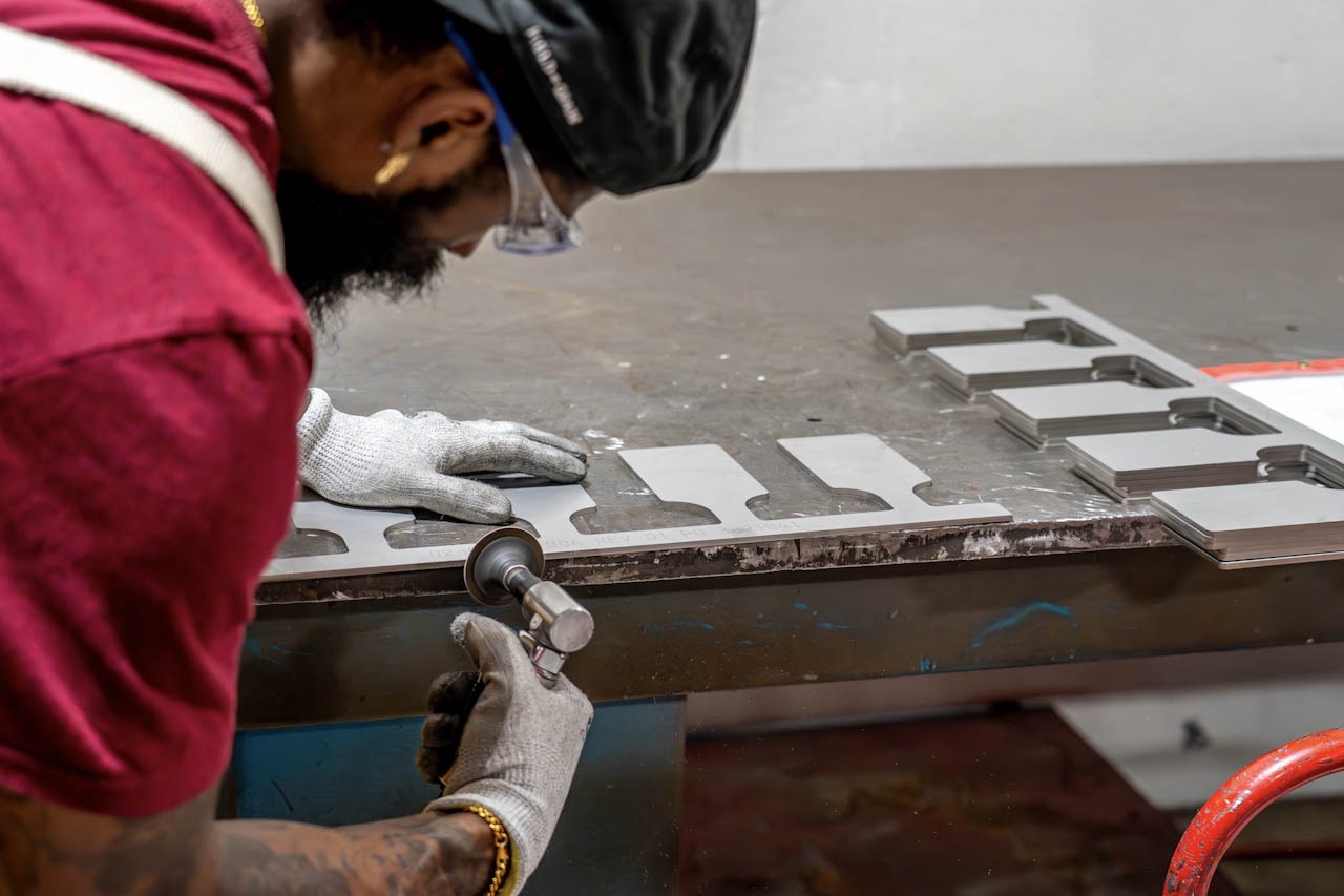 Technician deburring machined aluminum parts at a finishing bench in a Compass Precision facility