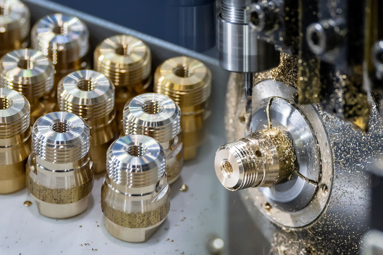 Rows of machined brass fittings beside a Swiss screw machine spindle